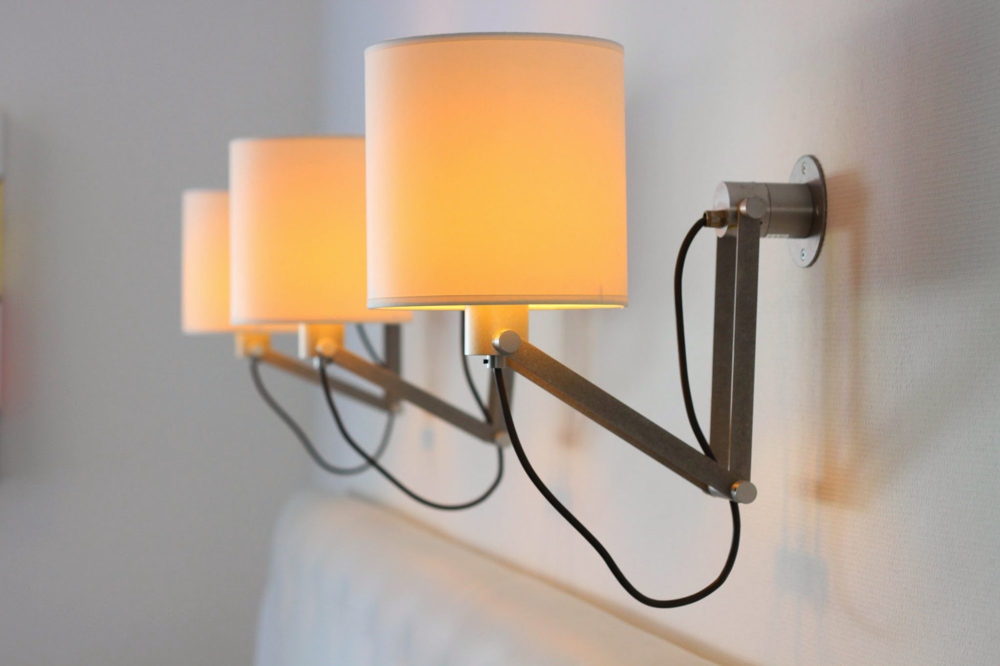 Drie wandlampen boven een bed, aangesloten en brandend